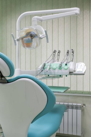 Eine moderne Zahnarztpraxis verfügt über einen eleganten blau-weißen Zahnarztstuhl. Das Metallgestell erstrahlt unter den Deckenleuchten und schafft eine saubere und professionelle Atmosphäre.