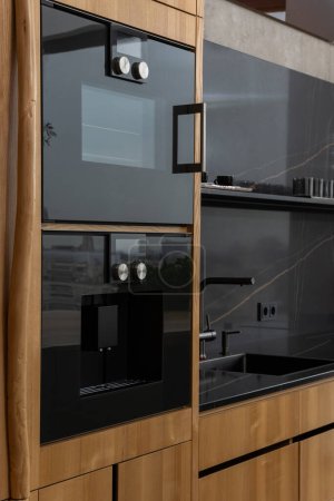 Foto de Una cocina con armarios de madera dura con un acabado en madera, complementado con electrodomésticos negros. Los estantes y accesorios añaden un toque moderno al espacio - Imagen libre de derechos