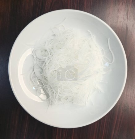 Téléchargez les photos : Nouilles de riz blanc dans une assiette blanche sur une table en bois, vue sur le dessus - en image libre de droit