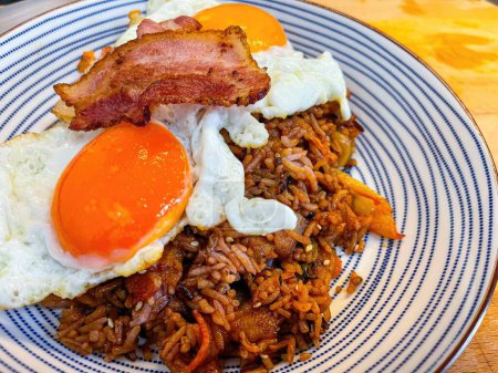 Fried rice with fried egg and bacon in a plate on wooden table