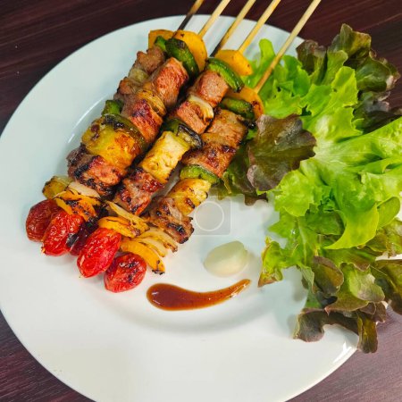 Téléchargez les photos : Viande grillée sur brochettes avec légumes sur une assiette blanche. - en image libre de droit