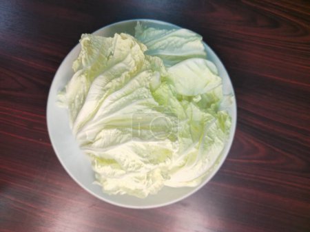 Téléchargez les photos : Chou chinois dans une assiette blanche sur une table en bois, vue de dessus - en image libre de droit