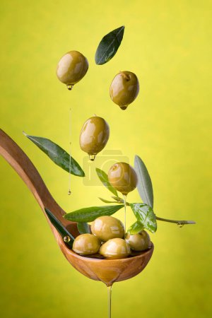 Téléchargez les photos : Louche aux olives et à l'huile sur fond vert. Des olives, de l'huile d'olive extra vierge et des feuilles d'olive flottent dans l'air - en image libre de droit