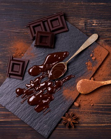 Foto de En primer plano, en un ambiente oscuro, cacao en polvo, trozos de chocolate negro y chocolate derretido - Imagen libre de derechos