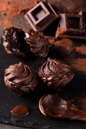 Foto de En primer plano, en un ambiente oscuro, algunos besos de chocolate, cacao en polvo y trozos de chocolate negro. - Imagen libre de derechos