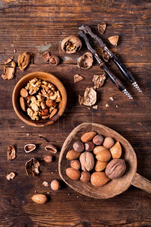 Téléchargez les photos : Seen from above, on an old wooden background, a nutcracker, a bowl with shelled walnuts and a wooden scoop contains mixed nuts - en image libre de droit