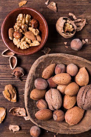 Foto de Top view, on an old wooden background, a bowl with shelled walnuts and a wooden scoop, in the foreground, contains mixed nuts. - Imagen libre de derechos