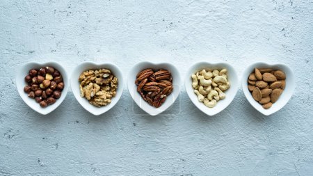 Photo for Top view, close up, on a textured white concrete background, five heart shaped bowls with shelled mixed nuts - Royalty Free Image