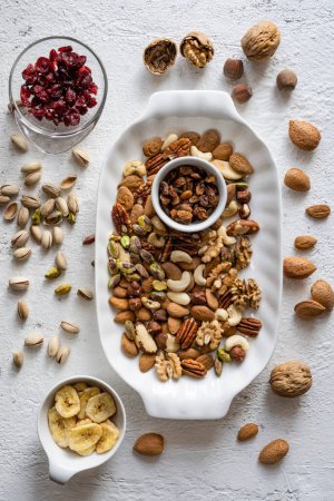 Foto de Top view, close-up, on a textured white concrete background, some bowls and a tray with mixed dried and dehydrated fruits - Imagen libre de derechos