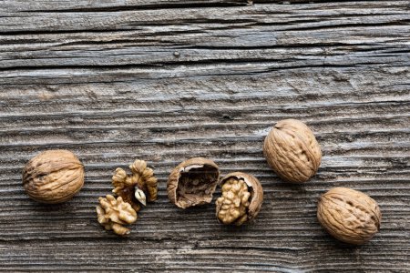 Photo for Top view, on an old wooden board, in the foreground, some walnuts with and without shell. Copy space. - Royalty Free Image