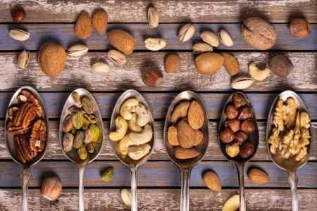 Foto de Top view, on a wooden background, a composition of mixed and shelled dried fruits is arranged in six vintage spoons, - Imagen libre de derechos