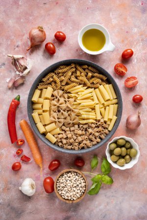 Téléchargez les photos : Poêle avec pâtes italiennes mélangées et une certaine variété de légumes sur un fond texturé - en image libre de droit