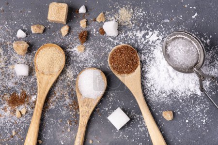 Foto de Sobre un fondo gris, diferentes tipos de azúcar refinado y a tanto alzado, blanco, crudo, aromatizado y en polvo - Imagen libre de derechos