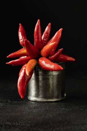 Photo for Spicy red chillies in an old metal measuring container on a black background. - Royalty Free Image