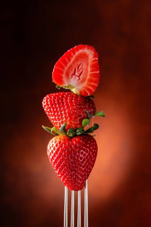 Foto de Tenedor con fresas de primer plano sobre fondo negro con brillo rojo. naturaleza muerta - Imagen libre de derechos