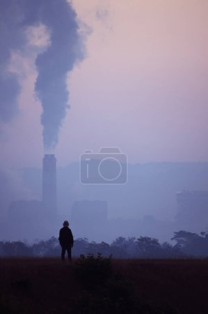 Téléchargez les photos : Silhouette d'un homme debout regardant une centrale au charbon Il y a de hautes cheminées qui émettent de la fumée de l'énergie de combustion de la pierre de transfert, concept de destruction de l'environnement réchauffement climatique. - en image libre de droit