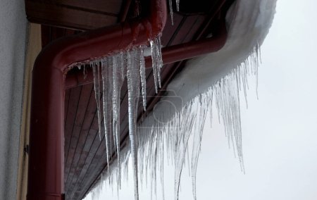 Foto de Winter icicles hanging from the roof and gutters ... - Imagen libre de derechos