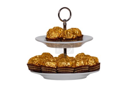 Photo for Pastries, desserts and sweets. Chocolate candies wrapped in golden foil on a two-storey etagere isolated on a white background. Clipping path. Decoration element for greeting card, poster or invitation. Macro. - Royalty Free Image