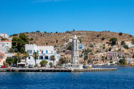 Foto de SYMI, Grecia - JUN 03, 2021. El puerto de Symi ciudad con los distritos de Chorio y Gialos es uno de los más bellos y románticos de todo el Egeo. Coloridas mansiones se extienden por las empinadas laderas. - Imagen libre de derechos
