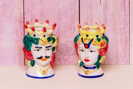 Photo pour Souvenir de Sicile. Pots ou vases traditionnels en céramique sicilienne avec les têtes d'un couple d'amateurs de têtes mauresques sur une table brillante et scintillante devant un mur en bois. - image libre de droit