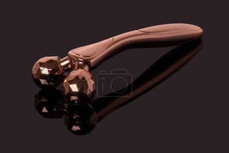 Photo for Skin care tools. A golden metal 3D face massager, face lift roller for better blood circulation and muscle activation on dark background. Beauty, skin treatment concept. - Royalty Free Image