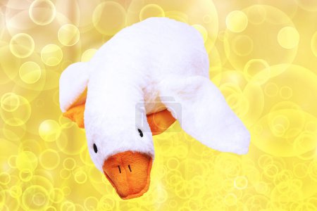 Soft white plush toy duck for kids over abstract yellow background. Duck teddy toy. White duck for playing.