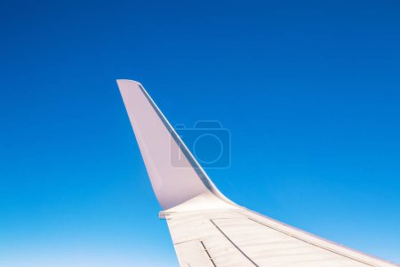 View at the part of a wing of the airplane or airliner during the flight from the window with blue sky and without clouds.Wing of aircraft.