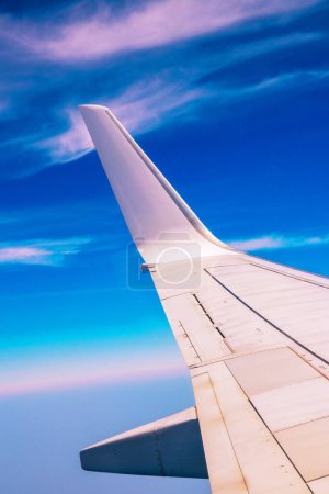 View of the part of a wing of an aeroplane or airliner in flight out of the window with blue sky and light clouds. Wing of aircraft. Copy space.