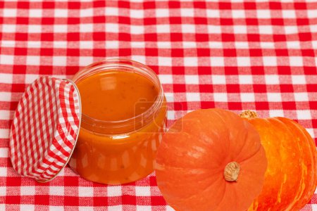 Photo for Natural cosmetics. Selective focus on a homemade pumpkin face mask in a glass jar and pumpkins on red checkered napkin. DIY cosmetics and SPA. Copy space. - Royalty Free Image