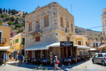 Foto de SYMI, Grecia - 03 JUNIO 2021. Una parrilla restaurante Symi ciudad cerca del puerto donde los turistas permanecen. Barrio más hermoso y romántico de todo el Egeo. - Imagen libre de derechos