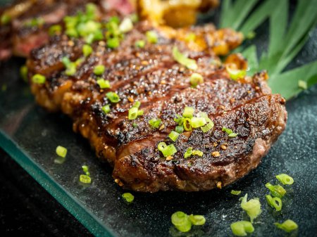 Photo for Close-up Australian sliced medium rare wagyu grilled beef steak top with sliced spring onion on glass plate on dark background, japanese style. Australian grilled meat texture. - Royalty Free Image