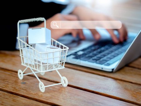 Produktsuche auf Online-Shopping-Shop-Anwendung im Internet mit Laptop-Computer, Online-Shopping-Konzepte. Suchmaschinen-Registerkarte virtuell auf dem Einkaufswagen mit Paketkästen auf dem Schreibtisch.