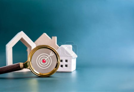House online search, property survey, buying, selling and real estate concepts. Target icon symbol in magnifying glass lens with many type style of house on blue background with copy space.