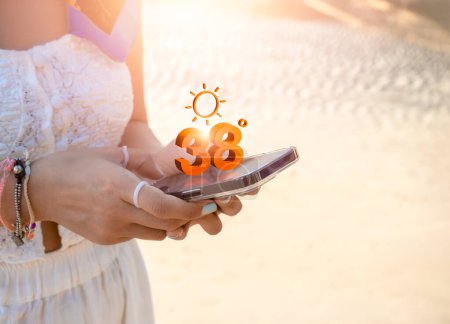 38 Grad Celsius, Wettervorhersage auf dem Smartphone. Hitzewetter, virtuelles Hochtemperatur-Display auf App mit Sonnensymbolen auf dem Smartphone-Bildschirm in der Hand auf Sandstrand-Hintergrund mit Kopierplatz.