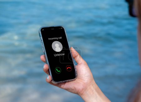 Eingehende Anrufe mit unbekannten Anrufern, böswillige Anrufe Konzept. Unbekannte Nummer zeigt auf Smartphone in der Hand einer Frau am Urlaubstag am Strand. Spam und Robocalls, Betrügeranruf-Alarm.