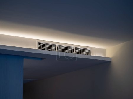 Klimaanlage wandmontiert Lüftungssystem an der Decke im weißen Hotelzimmer mit gedämpftem Licht. Hotelzimmer Lüftungsgitter an der Wand.