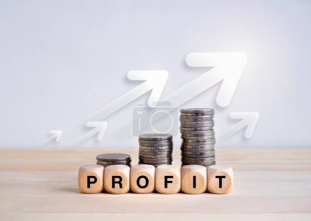 Business growth, revenue, investment, income, savings and balance concept. Text "PROFIT" on wooden cube blocks with money coin stacks graph steps with rising arrows on wood table and white background.