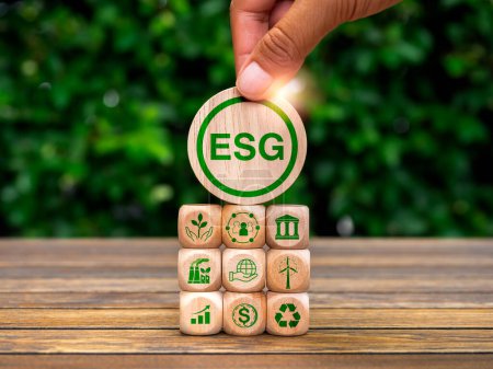 Environmental, social, and corporate governance (ESG), environment sustainable for save the earthconcept. Acronym text "ESG" in hand put on wood cube with icons on wood block stack, green background.