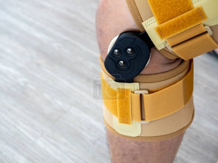 Photo for Close up yellow medical standard adjustable stabilised knee brace was worn on the knee of person, man who had injured his leg after playing sports. - Royalty Free Image