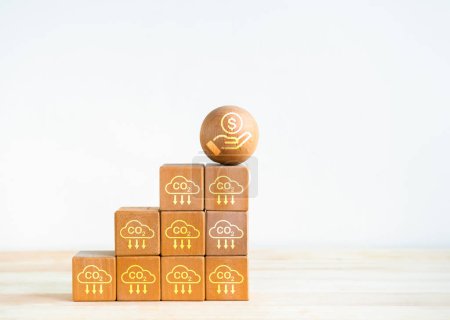 Carbon credit and Co2 emission reduction concept. Savings money icon on wood ball on top of wooden blocks steps as business growth graph with carbon emission reduction symbols on white background.
