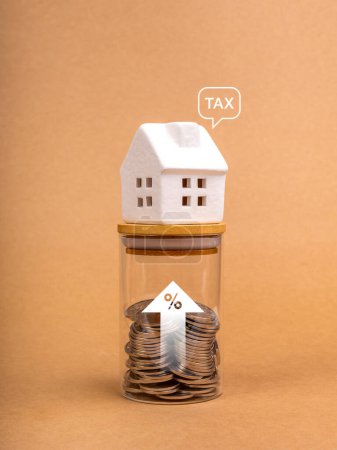 Eigenheimsteuer, Hypothekenzinsen, Immobilienfinanzierungskonzept. Wort "TAX" in Sprechblase auf weißem Haus auf Glasflasche mit Prozentsymbol und zunehmendem Pfeil mit Münzen innen, brauner Hintergrund.