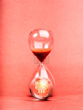 Global warming issue, Countdown to the crisis, environment sustainability concept. Co2 emissions reduction icon shining on glass earth globe near hourglass on red background, vertical style.