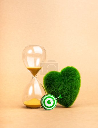 Environment sustainability, time and responsibility concept. Target of restoring our earth. 3d green target icon near hourglass and green grass heart shaped on vertical recycle paper background.