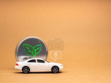 Elektroauto, Batterieladefahrzeug mit nachhaltigem Entwicklungskonzept. Plug-in-Symbol auf weißem Auto und grüner Pflanze, Öko-Symbol, Naturkraft auf Chrom-Plakette, brauner Hintergrund mit Leerzeichen.