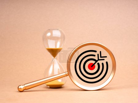 Photo for Short-term business goals encompass work that helps an organization reach its mid-term goals concept. Big target icon in gold magnifying glass lens near hourglass isolated on beige background. - Royalty Free Image
