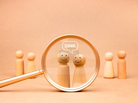 DINK concept, Double income, no kids or dual income, no kids, referring to couples who are voluntarily childless. Acronym text with wooden figures, happy male and female in magnifying glass lens.