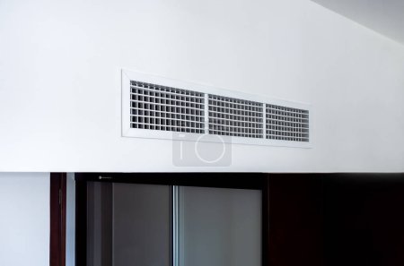 Side view of air conditioning wall mounted ventilation system on ceiling in the black and white hotel room. Hotel room air ventilation grill on the wall.