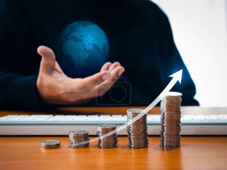 Investment online, taxable income, worldwide business jobs concept. Rising arrow on coin stacks as growth graph steps while businessman's hand holding virtual digital world globe on dark background.