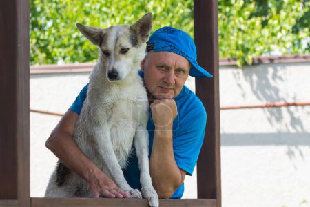 Photo for Nice outdoor portrait of Caucasian mature man and his cute young white  dog standing on summer veranda - Royalty Free Image