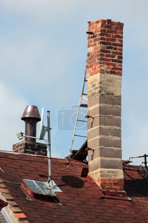 Alter Ziegelschornstein auf dem Dach mit einer Metallleiter zur Wartung